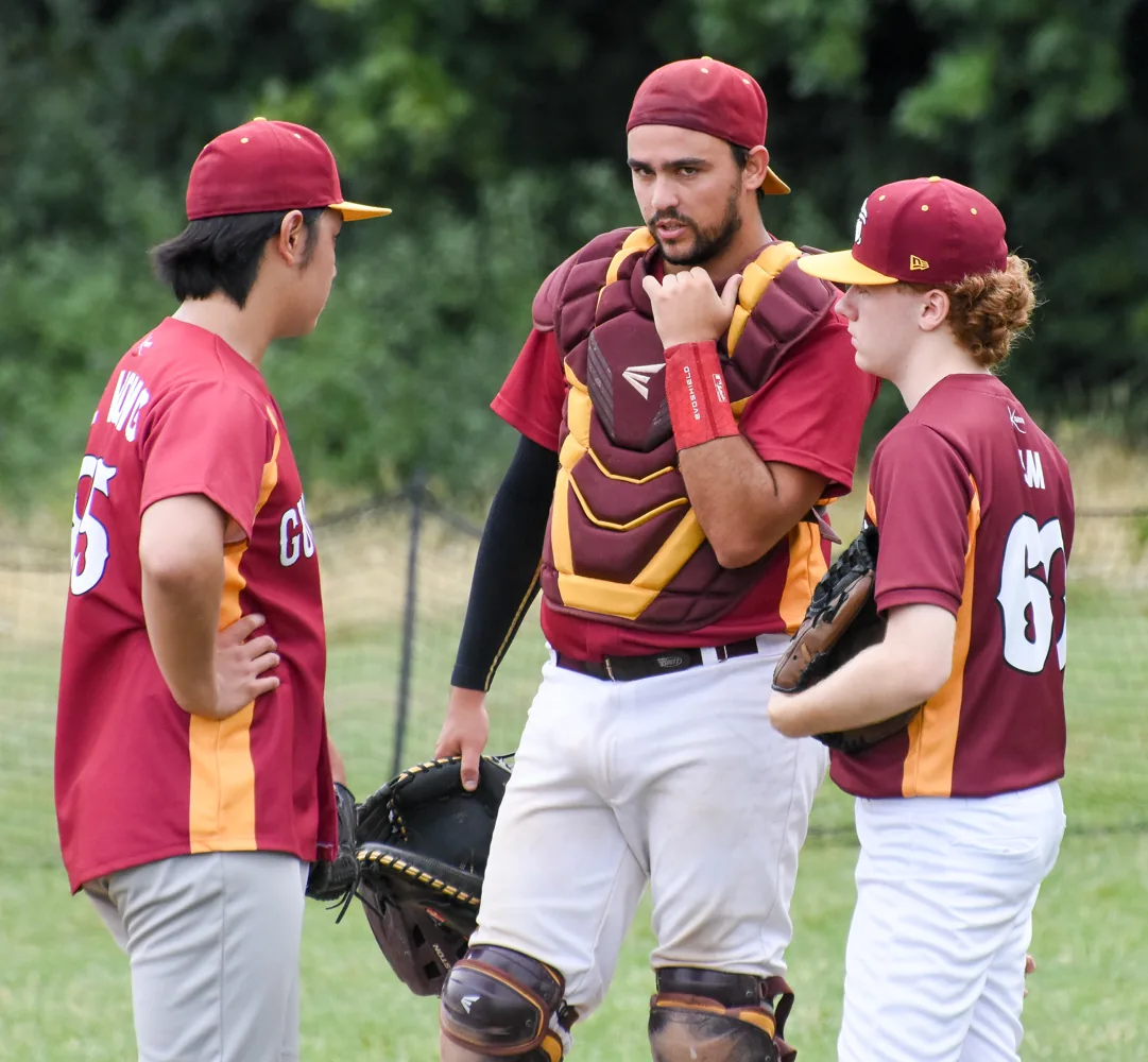 A Guildford catcher talks with two teammates on the field
