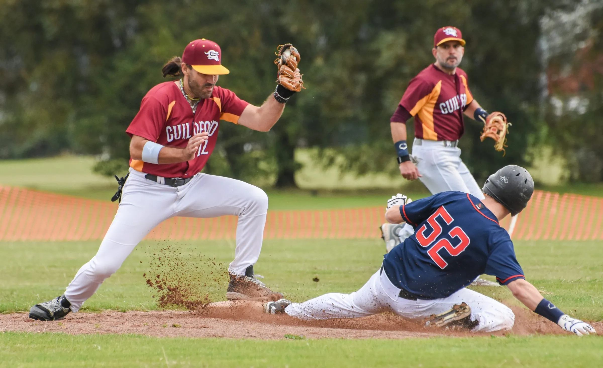 A Guildford fielder takes the throw as the runner slides into the base, dirt flying